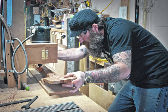 Chase Gullett in the workshop bent over a guitar neck guiding it through a table-mounted machine.