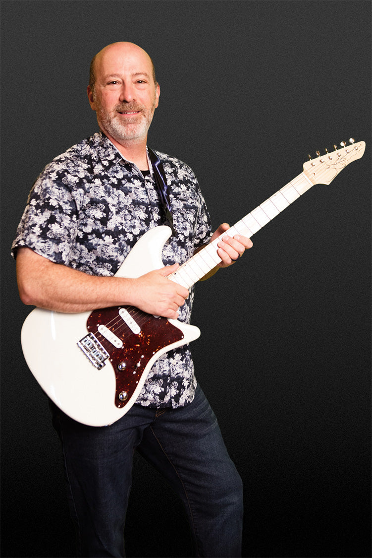 Peter Swartz, CEO of John Page Classic Guitars, standing on dark grey background holding a white Ashburn guitar.